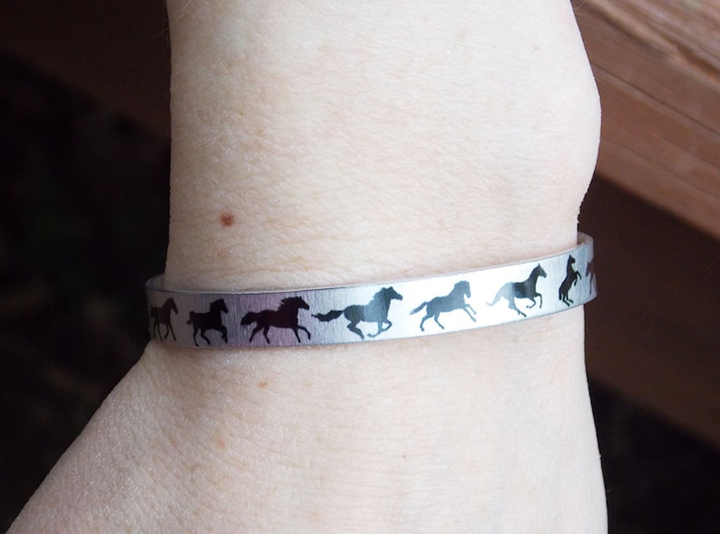May include: A silver bracelet with a row of black horse silhouettes running around the band.