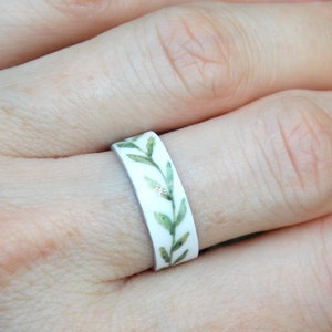 May include: A white ring with a green leafy design. The leaves are painted in shades of green and have a watercolor effect.