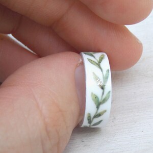 May include: A white ring with a green leafy design. The ring is made of washi tape and has a glittery finish.