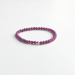 May include: A purple gemstone bracelet with a gold bead accent.