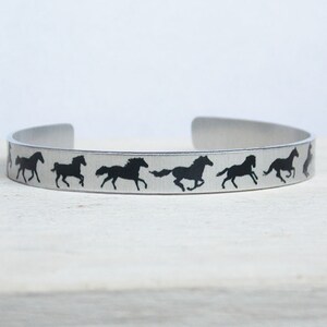 May include: A silver metal bracelet with a repeating pattern of black horse silhouettes running in a line.