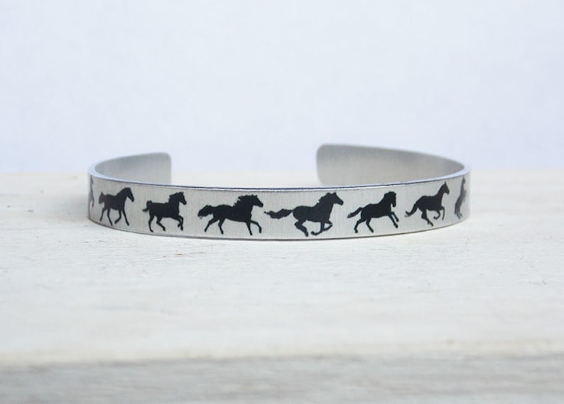 May include: A silver metal bracelet with a repeating pattern of black horse silhouettes running in a line.