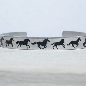 May include: A silver metal bracelet with a row of black horse silhouettes running in a circle.