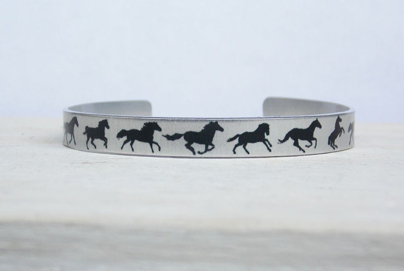 May include: A silver metal bracelet with a row of black horse silhouettes running in a circle.