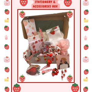 May include: A cardboard box filled with strawberry-themed stationery and accessories, including a notepad, pen, socks, scrunchie, stickers, beaded bracelets, hair clips, and earrings. The box features the text STRAWBERRY THEMED STATIONERY & ACCESSORIES BOX.