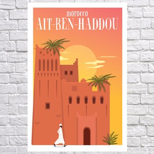 May include: A colorful illustration of a traditional Moroccan building with a person walking in front of it. The building is made of red brick and has a tall tower with windows. The sky is orange and yellow, and there are palm trees in the foreground. The text "MOROCCO A&Iuml;T-BEN-HADDOU" is at the top of the image.