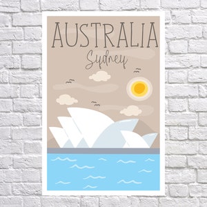 Puede incluir: Un p&oacute;ster con la &Oacute;pera de S&iacute;dney, con el texto "AUSTRALIA Sydney". La obra de arte incluye una escena de agua azul, un sol amarillo, nubes y p&aacute;jaros sobre un fondo beige. El p&oacute;ster se muestra contra una pared de ladrillos blancos.