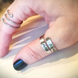 May include: Two silver rings on a finger. The ring on the thumb has Hebrew writing on it. The other ring is a spiral with two small clear stones.