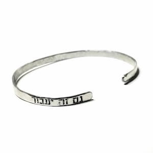 May include: A silver bangle bracelet with the Hebrew words "Gam Zu Ya'avor" engraved on it, which translates to "This too shall pass".