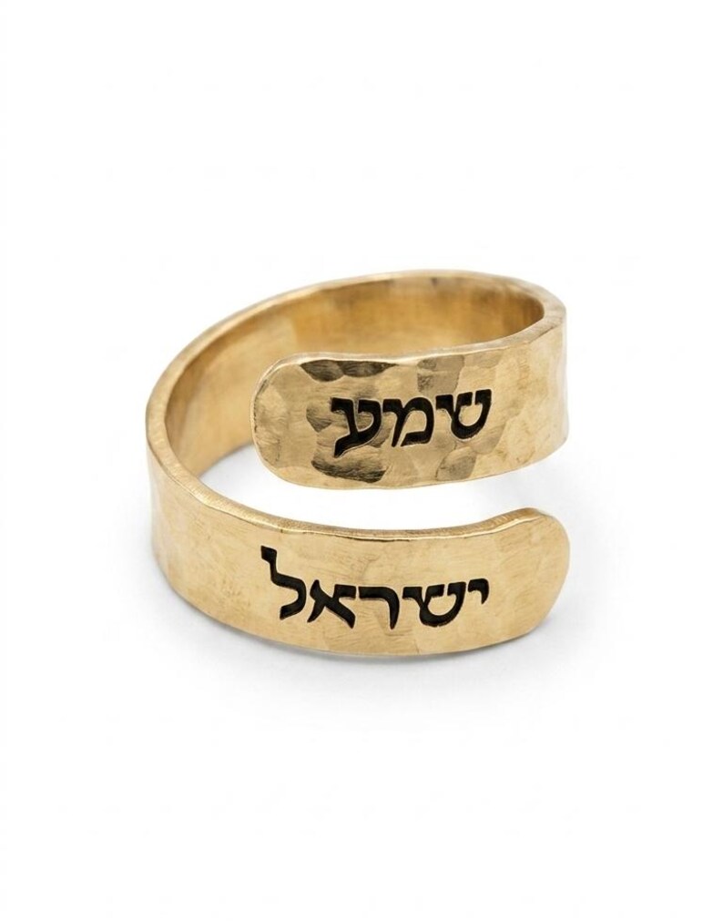 May include: A gold-toned bypass ring featuring a hammered texture on the metal surface. The ring displays black Hebrew text engraved on both ends of the open band, with the word 'שמע' on the upper section and 'ישראל' on the lower section.