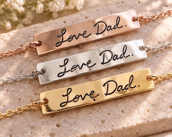 Puede incluir: Tres pulseras de barra metálica en tonos oro rosa, plata y oro. Cada barra rectangular presenta el texto cursivo negro grabado Love Dad. Las pulseras están unidas a cadenas de eslabones metálicos a juego y se muestran horizontalmente.