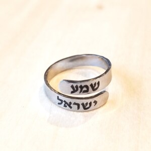 May include: A silver ring with the Hebrew words "Shalom" and "Shabbat" engraved on it.