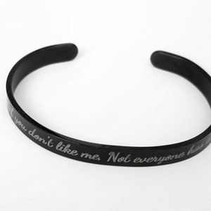 May include: Black metal bangle bracelet with the engraved text "If you don't like me, Not everyone has to."