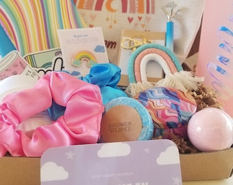 May include: A gift box filled with rainbow-themed items, including a rainbow keychain, a bath bomb, a shower steamer, a hair scrunchie, a sticker, and a card that says "I believe in you!"
