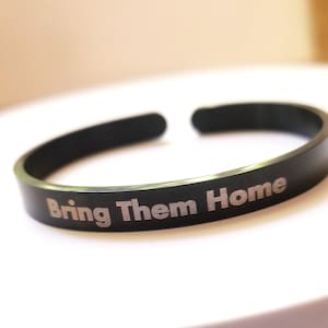 May include: A black metal bracelet with the words "Bring Them Home" engraved in silver lettering.