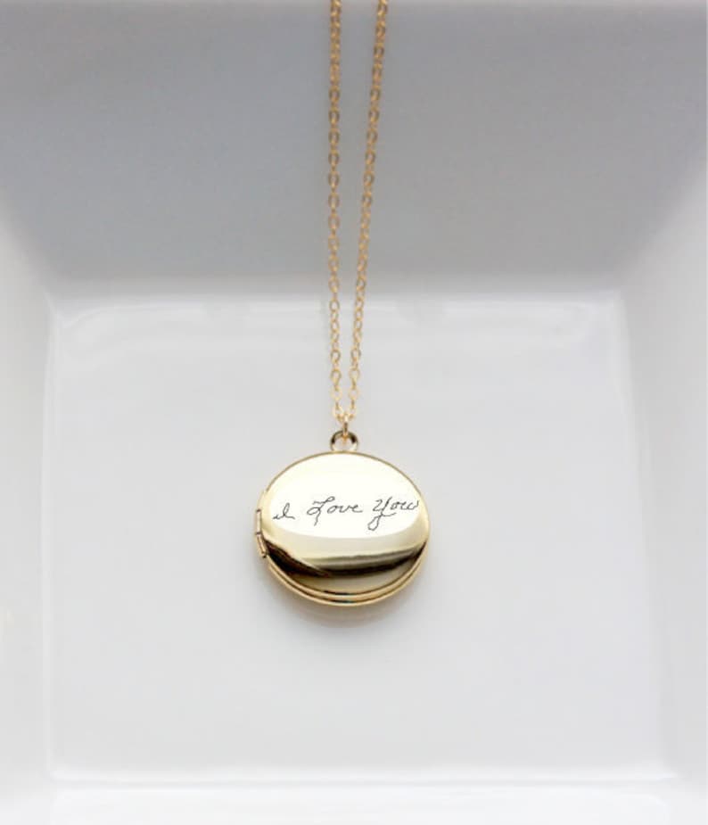 May include: A gold chain necklace with a round locket pendant. The locket is engraved with the handwritten message "I love you".