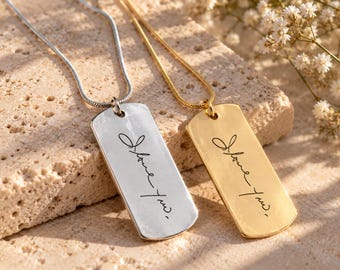 Puede incluir: Dos colgantes rectangulares tipo placa militar en cadenas finas, uno en tono plateado y otro en tono dorado. Cada colgante presenta el texto grabado en cursiva "I love you," con una coma al final. Los colgantes son lisos.