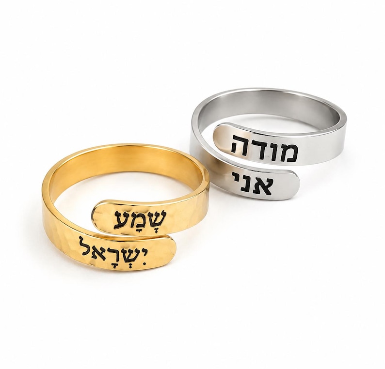 May include: Two adjustable wrap rings, one gold-toned and one silver-toned, featuring hammered metal bands. The gold ring is engraved with the Hebrew text "שמע ישראל" in black, while the silver ring is engraved with the Hebrew text "מודה אני" in black.