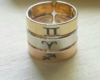 May include: Three stacked gold, silver, and rose gold rings with zodiac symbols engraved on them. The top ring has the Gemini symbol, the middle ring has the Aries symbol, and the bottom ring has the Sagittarius symbol.