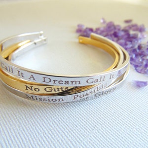 May include: Three silver and gold bangle bracelets with engraved inspirational messages: "Call it a dream call it", "No guts no glory", and "Mission possible".