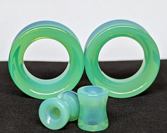 May include: A set of three green and blue glass ear gauges. The two larger gauges are circular and have a swirling pattern. The smaller gauge is cylindrical.