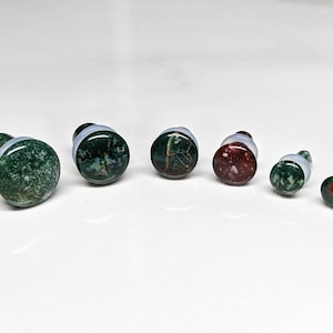 May include: Set of six green and red stone ear gauges, ranging in size from small to large. The gauges are made of polished stone with a natural marbled pattern.