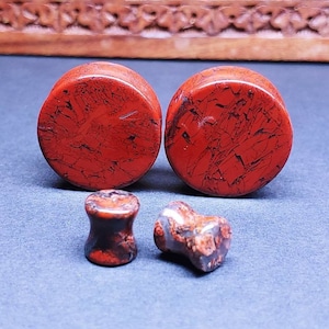May include: Set of four red and black stone ear gauges. The gauges are round and have a speckled pattern.
