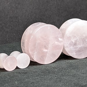 Puede incluir: Conjunto de cuatro dilatadores de oreja de cuarzo rosa. Los dilatadores son de diferentes tamaños, siendo el más grande de aproximadamente 2,5 cm de diámetro.