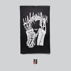 May include: Black and white patch featuring a stylized illustration of a character holding a card with an hourglass design. The word "HAHA" is repeated in the background. The character is wearing a suit and has a skeletal hand.