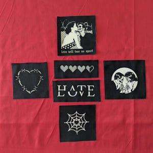 May include: Several black fabric patches with white designs are arranged on a red background. The patches feature images of couples, hearts, and a spiderweb. Text includes "Love will tear us apart" and a "HATE LOVE" design.