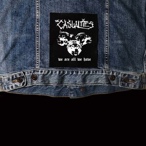 May include: Black and white patch with the text "The Casualties" and "We are all we have" with a graphic of three wolf heads.
