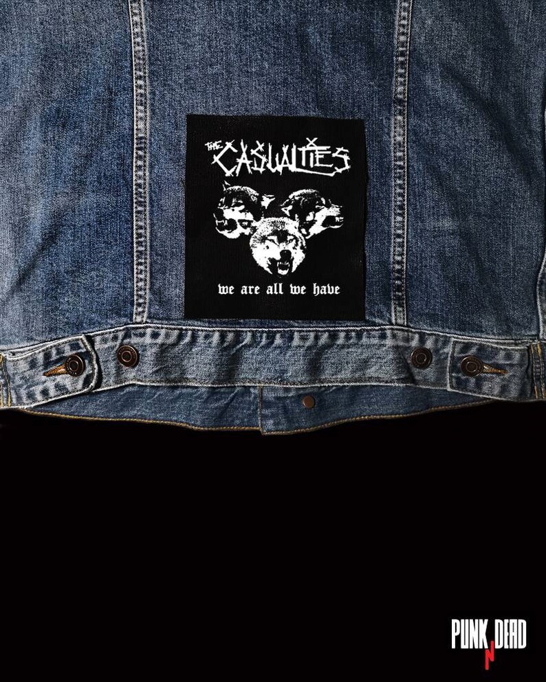 May include: Black and white patch with the text "The Casualties" and "We are all we have" with a graphic of three wolf heads.