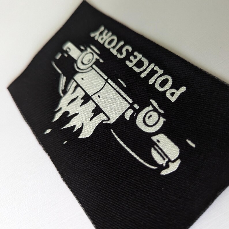 May include: Black fabric patch with white text that reads "POLICE STORY" and a white silhouette of a car on fire.