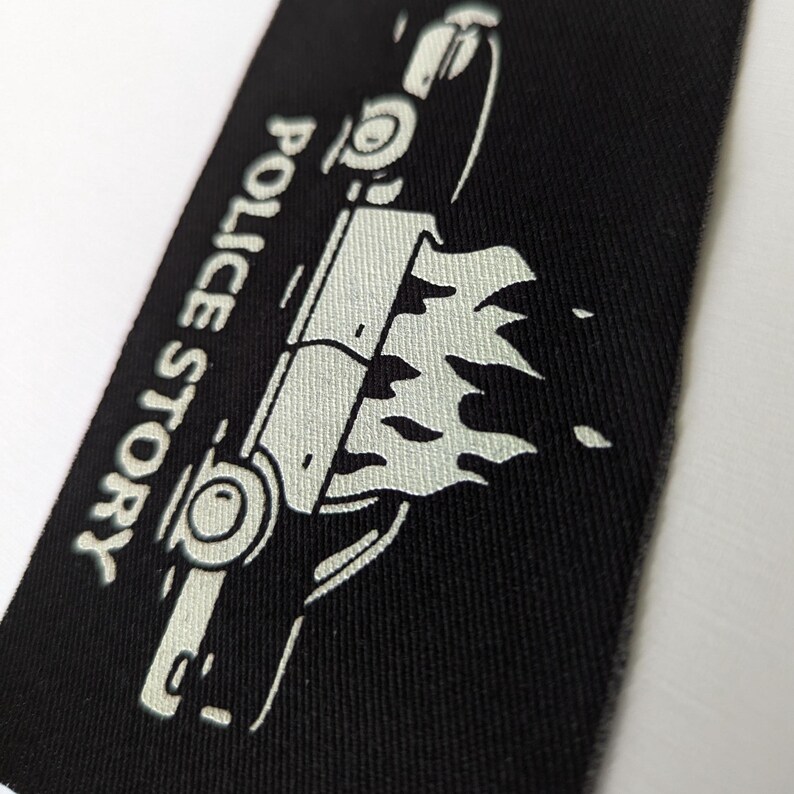 May include: A black patch with a white outline of a car on fire. The text "Police Story" is written vertically on the left side of the patch.
