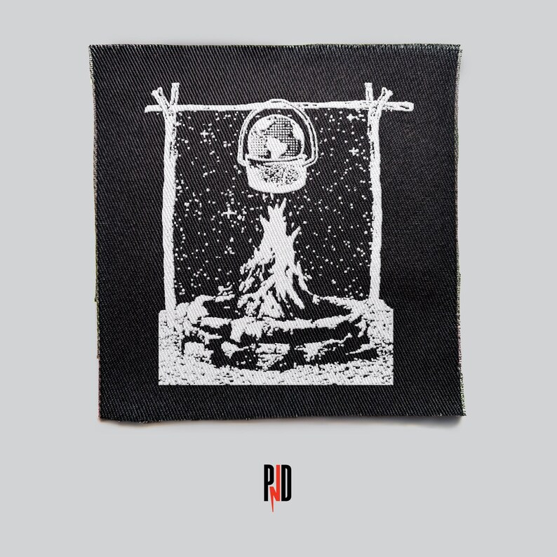 May include: A black and white embroidered patch depicting a campfire with a pot hanging above it. The background is a starry night sky. The patch is rectangular and has a rough, textured surface.