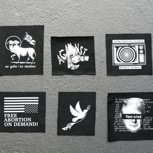 Puede incluir: Seis parches cuadrados negros con gráficos y texto blancos. Los diseños incluyen un cordero con una bandera, la palabra "AGAINST", un televisor con el texto "stop making stupid", una bandera estadounidense con "FREE ABORTION ON DEMAND!", una paloma y una cara con la palabra "fascist".
