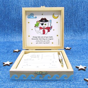May include: A wooden box with a blue and white wave design on the bottom. The lid is open and shows a cartoon tooth with an eye patch and a pirate hat. The tooth is holding a toothbrush and a parrot is perched on its shoulder. The text on the lid reads: "Always take care of your teeth, Remember that they are magical... every time you smile, you warm my heart!"