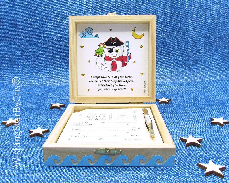 May include: A wooden box with a blue and white wave design on the bottom. The lid is open and shows a cartoon tooth with an eye patch and a pirate hat. The tooth is holding a toothbrush and a parrot is perched on its shoulder. The text on the lid reads: "Always take care of your teeth, Remember that they are magical... every time you smile, you warm my heart!"