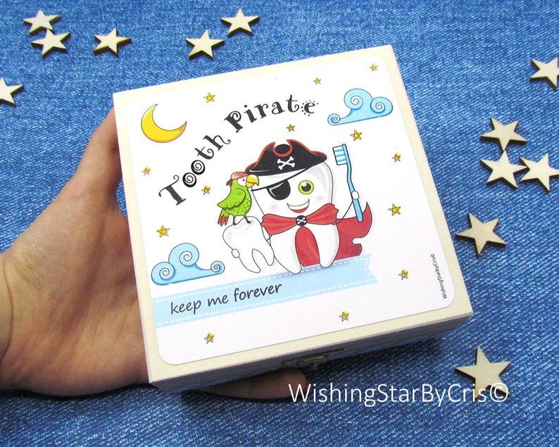 May include: A white wooden box with a colorful illustration of a tooth pirate holding a toothbrush. The box has the text "Tooth Pirate" and "keep me forever" on it. The box is perfect for storing lost teeth.