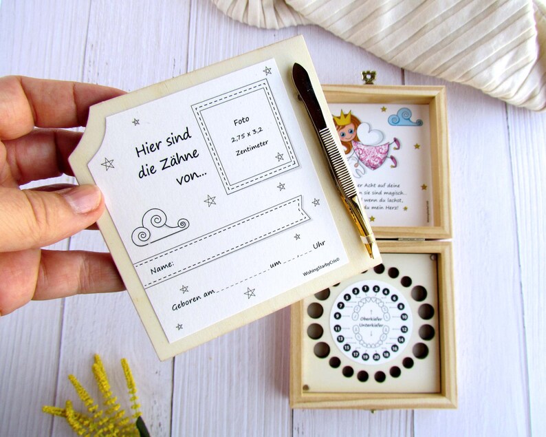 May include: A wooden box with a tooth fairy theme. The box has a compartment for storing baby teeth and a chart to track when each tooth falls out. The box also includes a small pair of tweezers and a space for a photo. The text on the box reads "Here are the teeth of..." and includes space to write the child's name and birthdate.