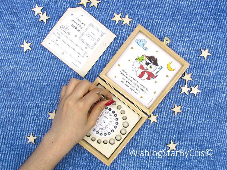 May include: A wooden box with a tooth fairy theme. The box has a compartment for storing baby teeth and a removable card with a tooth chart. The card also has a space for a photo and a message. The box is decorated with a pirate tooth character and the text "Always take care of your teeth, Remember that they are magical! Every time that you smile, you warm my heart."