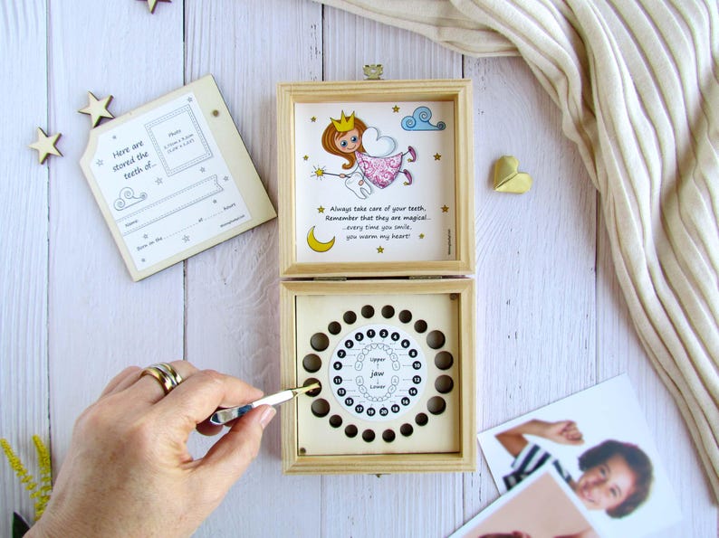 May include: A wooden box with a tooth fairy illustration on the lid. The box has a chart inside for storing baby teeth. The text on the lid reads "Always take care of your teeth. Remember that they are magical. Every time you smile, you warm my heart."