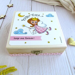 May include: A wooden box with a pink and white tooth fairy design. The box has a small latch and a pink lace trim. The text on the box reads "Tooth Fairy keep me forever!"