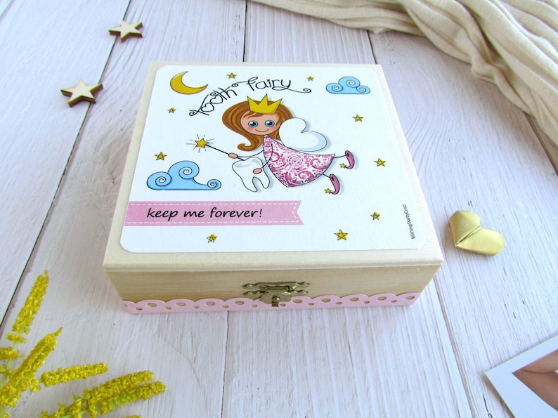 May include: A wooden box with a pink and white tooth fairy design. The box has a small latch and a pink lace trim. The text on the box reads "Tooth Fairy keep me forever!"