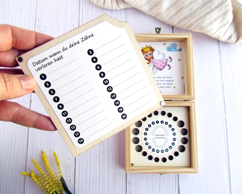 May include: A wooden box with a chart to track when a child loses their baby teeth. The chart has numbers 1 through 20. The box also has a compartment for storing lost teeth. The box has a fairy illustration with the text "When you lose a tooth, fairies are magic, they come to you at night, when you sleep, and take your tooth, and leave you a gift, my dear!"