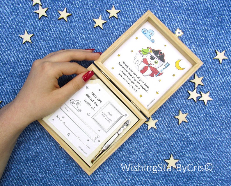 May include: A wooden box with a white card inside. The card has a cartoon illustration of a tooth with a pirate hat and a toothbrush. The text on the card reads "Always take care of your teeth, remember that they are magical... every time you smile, you warm my heart!" The box is open and there is a smaller white card inside with the text "Here are stored the teeth of..." and a space for a photo and information about the child.
