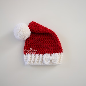 Puede incluir: Un gorro de Pap&aacute; Noel rojo y blanco tejido a ganchillo, con un pomp&oacute;n blanco y un lazo blanco. El gorro est&aacute; hecho a mano y presenta el texto "Canyon View Crochet" y "CanyonViewCrochet.etsy.com".