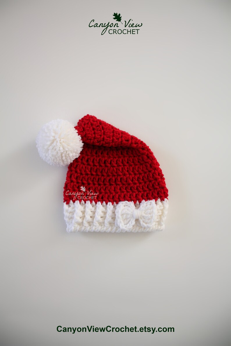 Puede incluir: Un gorro de Pap&aacute; Noel rojo y blanco tejido a ganchillo, con un pomp&oacute;n blanco y un lazo blanco. El gorro est&aacute; hecho a mano y presenta el texto "Canyon View Crochet" y "CanyonViewCrochet.etsy.com".
