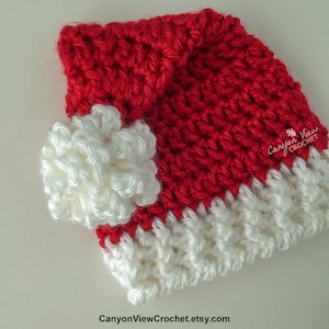 May include: Red and white crocheted Santa hat with a white pom-pom. The hat has a fold-over brim and is made with a textured stitch.