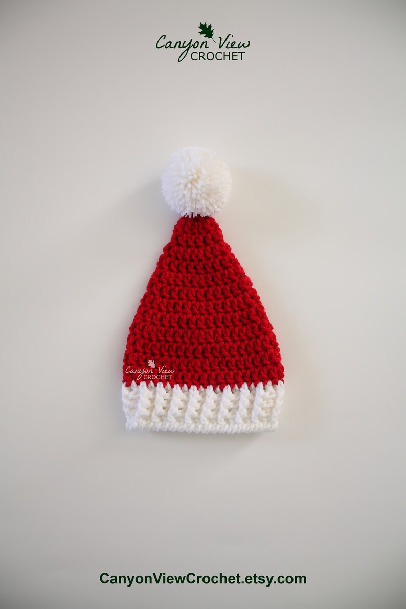 Puede incluir: Un gorro de Pap&aacute; Noel rojo y blanco tejido a ganchillo, con un pomp&oacute;n blanco. El gorro tiene un borde blanco acanalado y est&aacute; hecho de hilo texturizado. El texto "Canyon View Crochet" y "CanyonViewCrochet.etsy.com" son visibles.